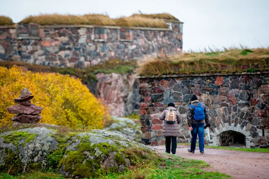 Image of two people walking in Suomenlinna fortress with the stone walls in the background.